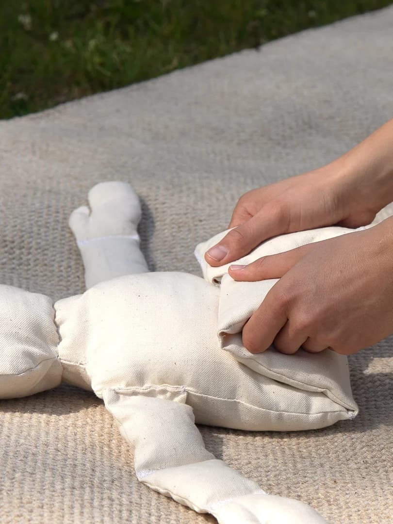 Andri's hands guiding a teaching doll's bent legs in the Knee-to-Chest demonstration