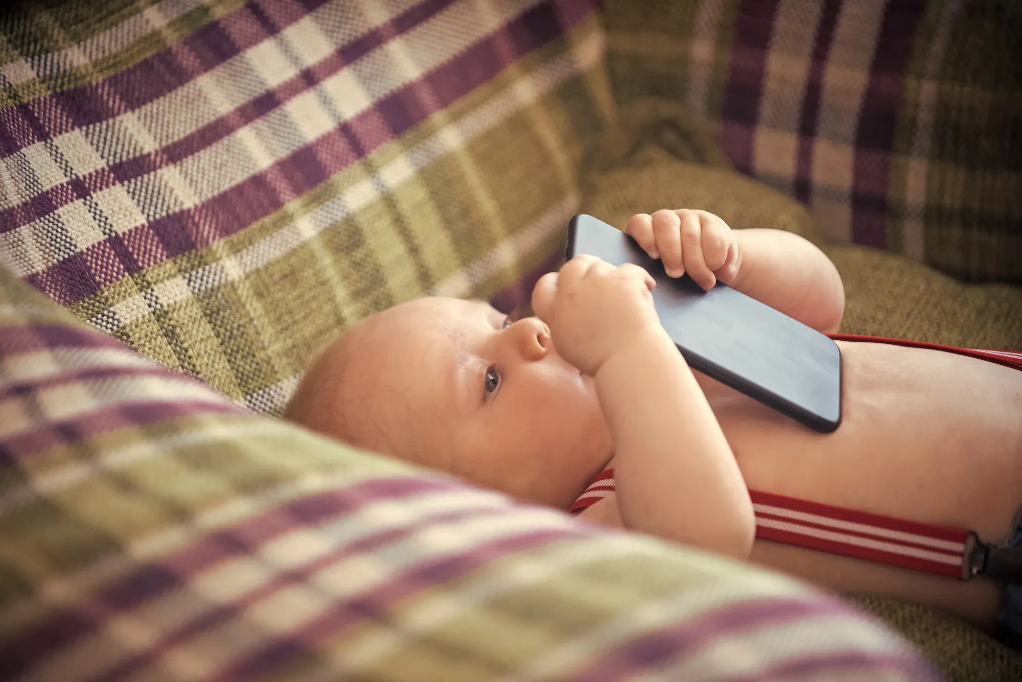 Baby studying smartphone in armchair