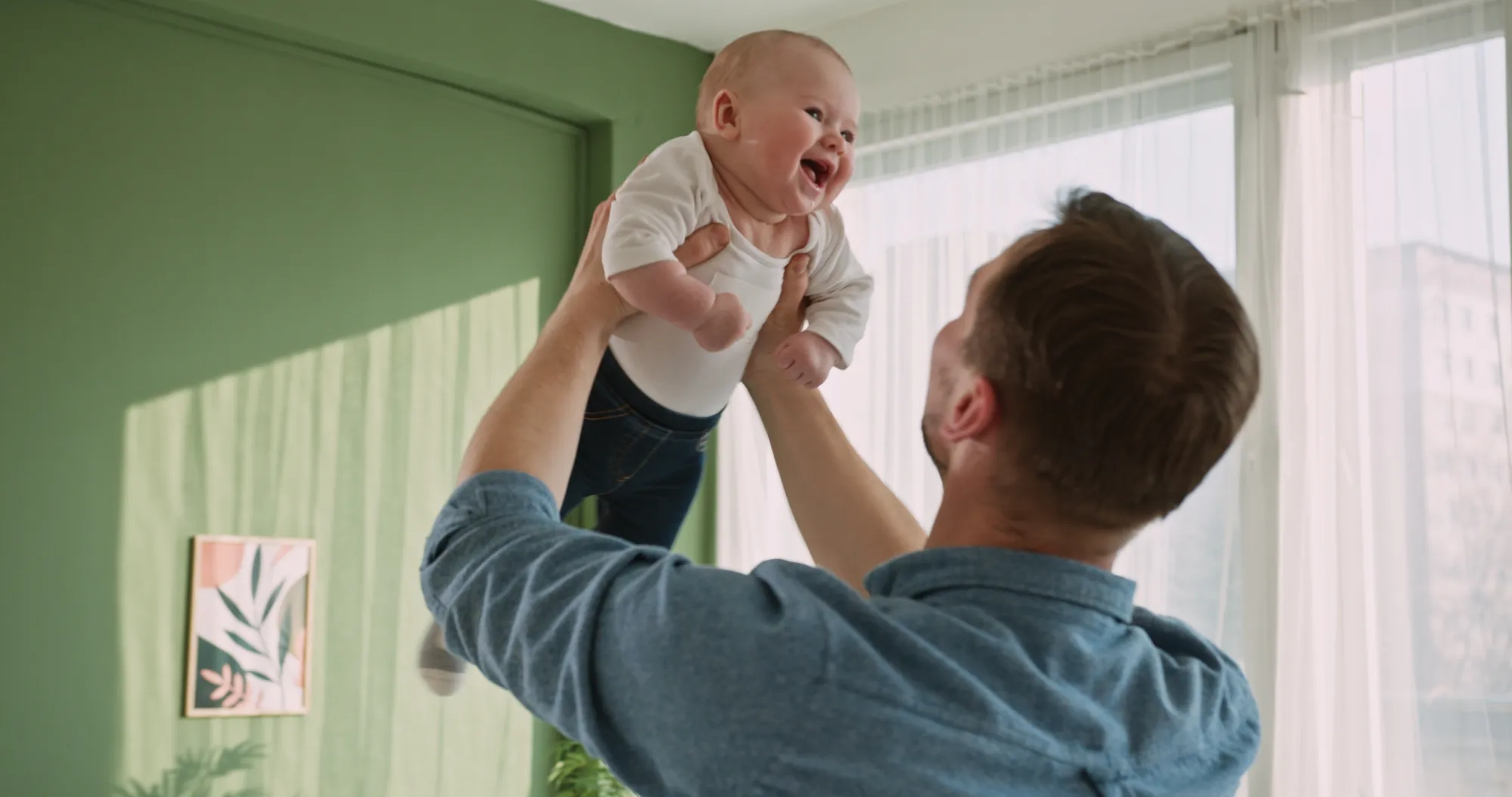 Exuberant baby laughing while being lifted by father