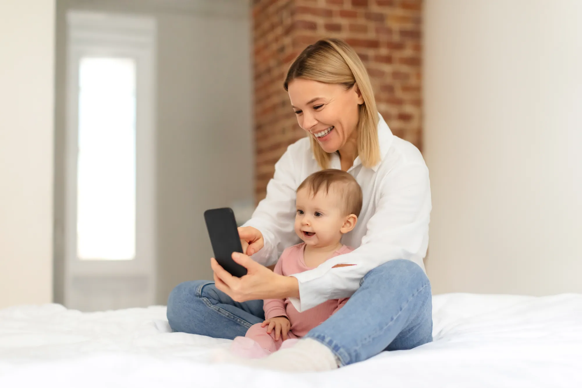 Mother and infant using cellphone in bedroom