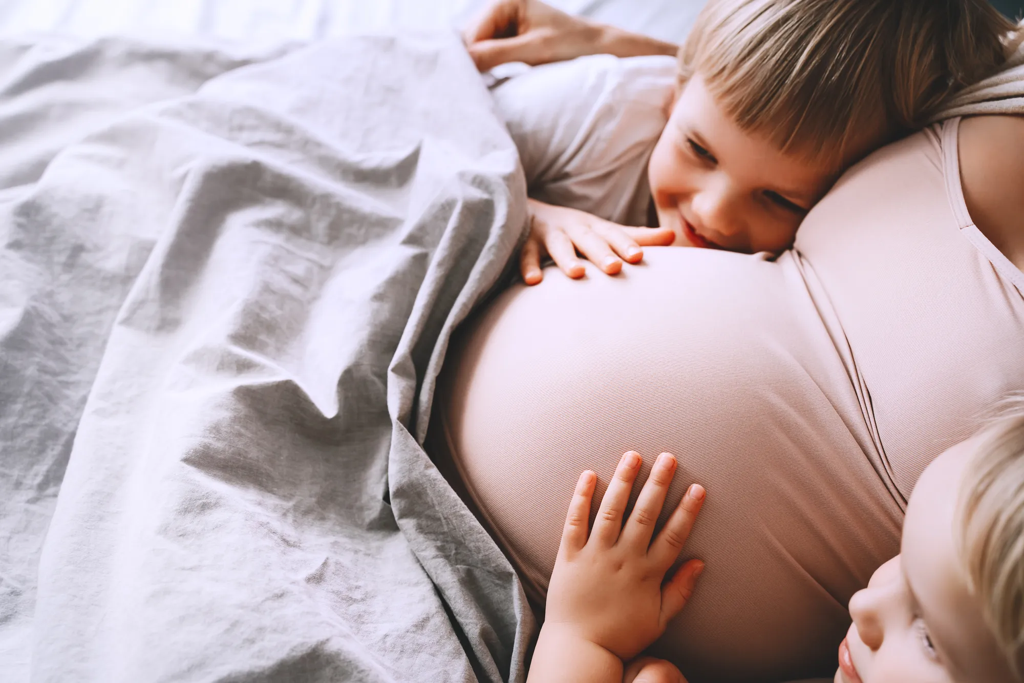 Toddler holding pregnant mother's belly in intimate home moment